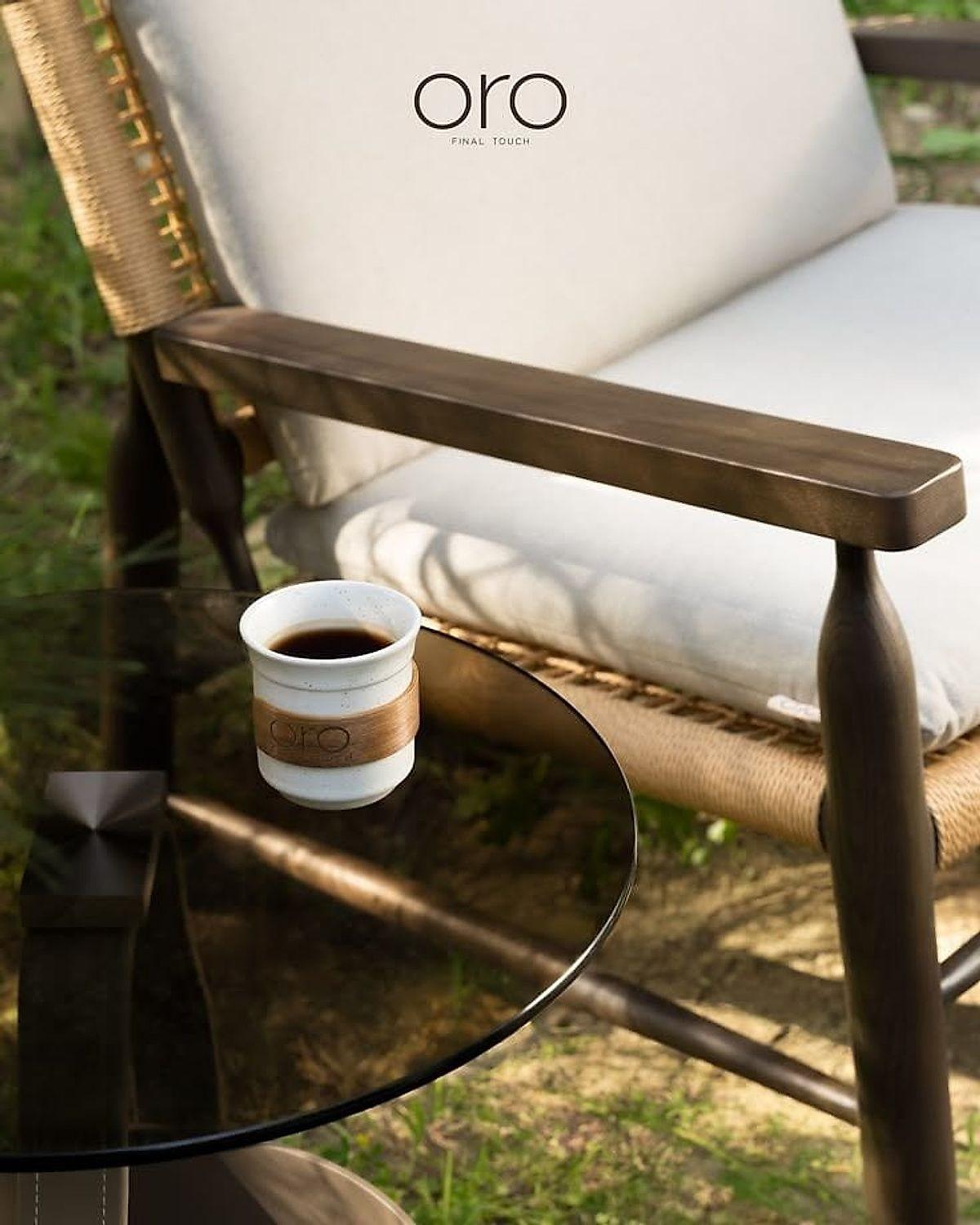 A cup of coffee resting on the wide timber arm of a cane chair, hill light behind