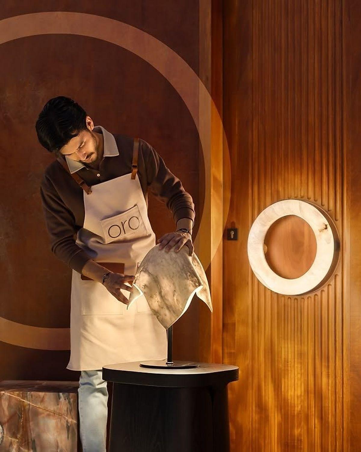 A maker lifting the finished alabaster veil against a timber wall