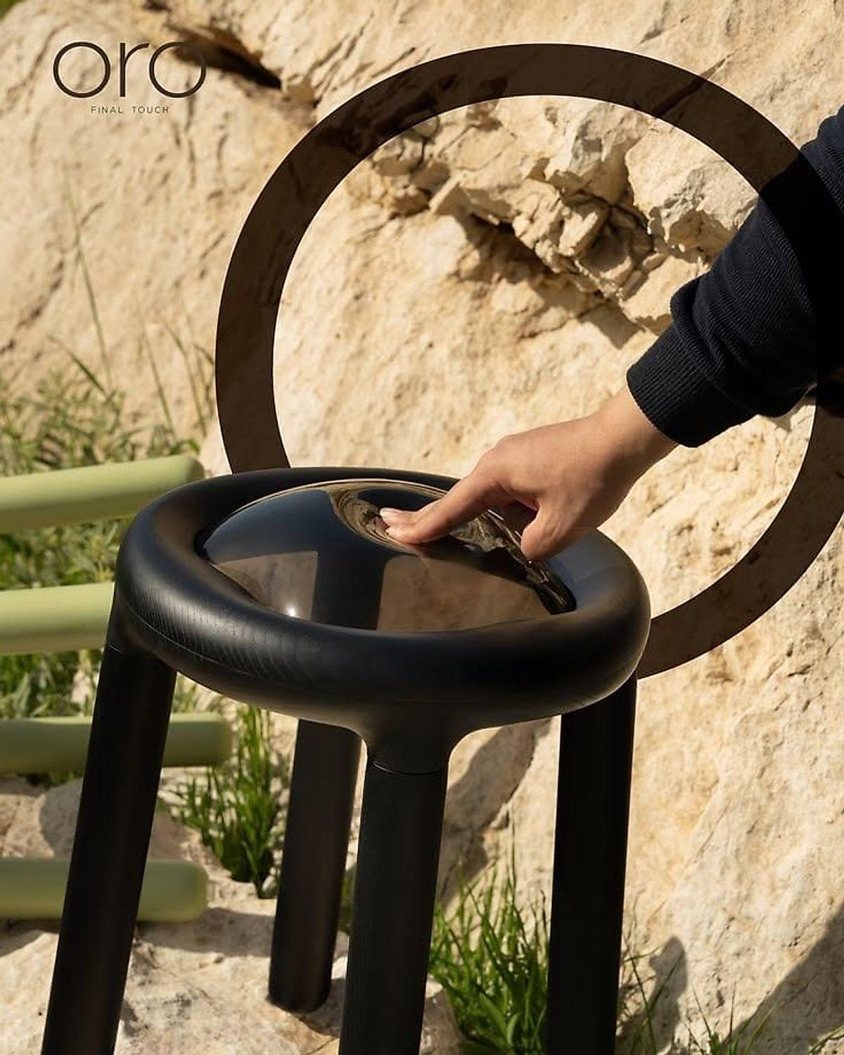 A hand steadying a black tubular stool set on bare rock outdoors